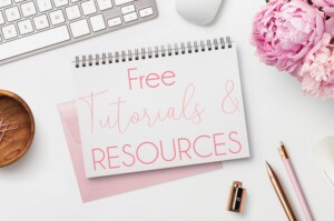 A desk with a notepad reading "free tutorials & resources," accompanied by a pink peony, a wooden bowl, pens, a keyboard, and a notepad. A clean, professional setting with