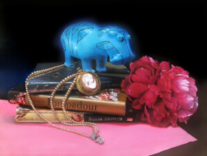A whimsical, blue, ornately patterned elephant figurine stands atop stacked books titled "Madame de Pompadour" by Susan Griffin, accented with a pink scarf, a pearl necklace