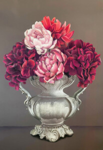 An elegant silver vase with ornate handles hosts a whimsical bouquet of pink, red, and deep purple flowers against a muted background.