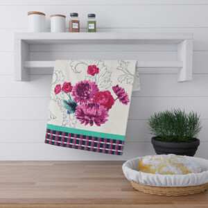 A modern kitchen countertop with a floral-patterned towel hanging on a white wooden rack, flanked by a potted green plant on the right and a basket containing bread on the left, reminiscent of