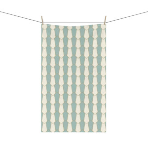 A whimsical, light teal towel with a white geometric pattern, hanging from a clothesline by two clothespins, isolated on a white background.