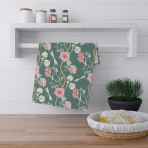 A kitchen counter featuring a whimsical bread basket with a loaf, next to a potted plant, under a shelf with jars and a floral patterned cloth hanging from it.