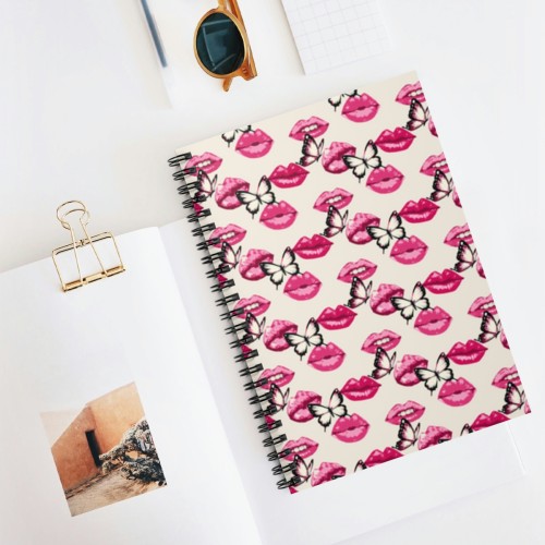A Lip Service in Pink Spiral Notebook - Ruled Line with a whimsical lip print design next to sunglasses and a binder clip holding a small photo, placed on a white surface.