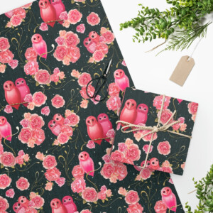 Joyful Owls Wrapping Paper featuring a whimsical pink owl and rose floral pattern on a dark background, scissors, twine, and greenery on a white surface. A blank tag is also visible.