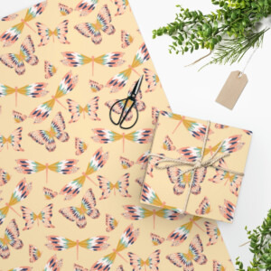 Flat lay of Flying Cuties in Gold Wrapping Paper and notebooks with a surrealism butterfly print design, alongside scissors, a sprig of greenery, and a blank tag, on a plain white background.