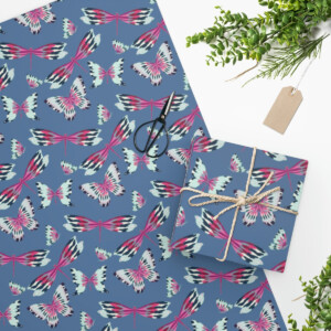 Top view of a gift wrapped in Custom Wrapping Paper with a colorful butterfly pattern, accompanied by scissors, a green plant, and a blank tag featuring surrealism artwork by Las Vegas artist Melanie Stimmell.