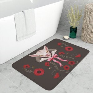 A whimsical bathroom floor mat featuring an illustration of a sphynx cat wearing a pink bow surrounded by a floral pattern, placed next to a bathtub and a woven basket.