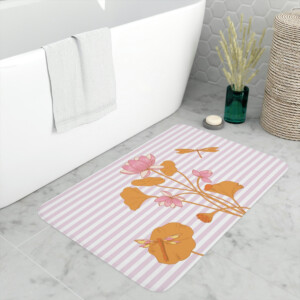 A stylish bathroom featuring a modern white bathtub, with a pink and white striped bath mat adorned with floral designs on the floor. Decorative elements include a Melanie Stimmell painting and a green bottle.