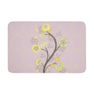 A decorative bath mat featuring a stylized tree with yellow and white flowers on a soft pink background patterned with light purple circles and surreal lattice designs.