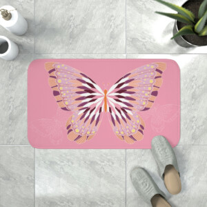 A whimsical decorative bath mat with a large, intricate butterfly design in shades of pink and taupe, viewed from above with a pair of gray slippers at the edge and a plant nearby.