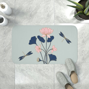 A whimsical bath mat featuring a stylized floral design with pink flowers, blue leaves, and dragonflies, placed on a tiled bathroom floor with a pair of grey slippers positioned at the bottom edge